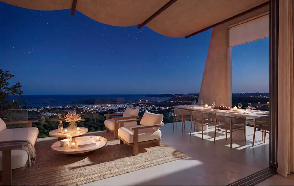 Terraza cubierta de noche con salón exterior y comedor frente a la bahía